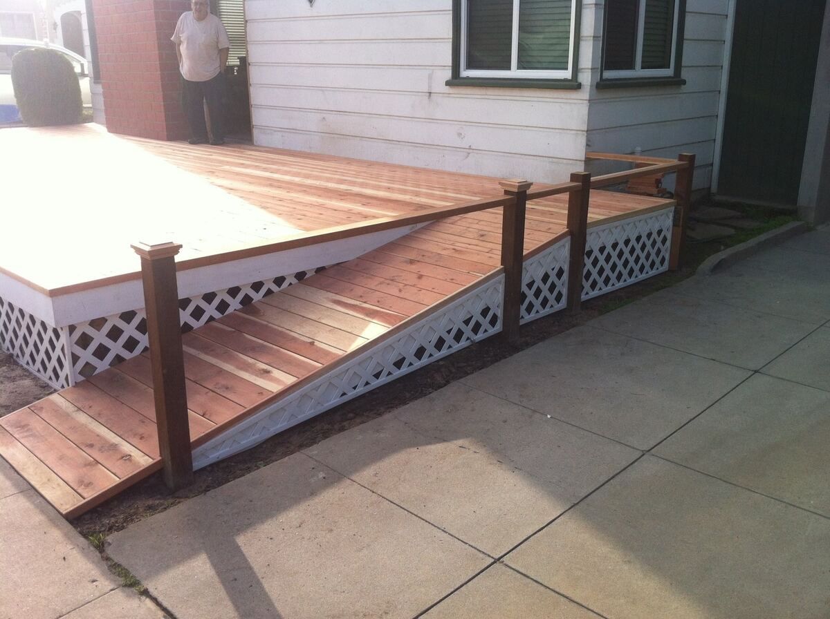 Wooden access ramp with a continuous handrail running along the side of a residential building