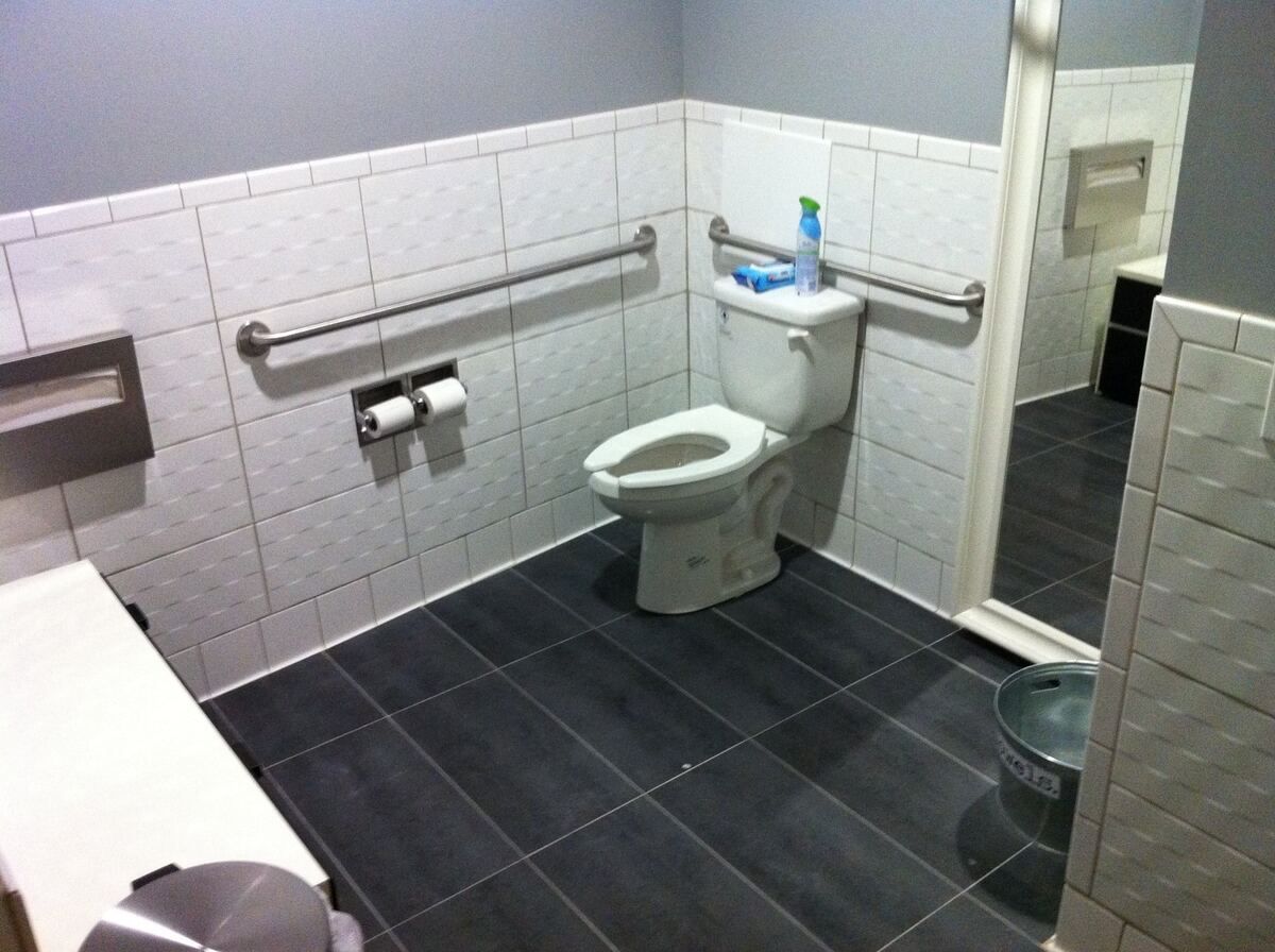 Commercial restroom with rear and side-wall grab bars beside a comfort-height toilet