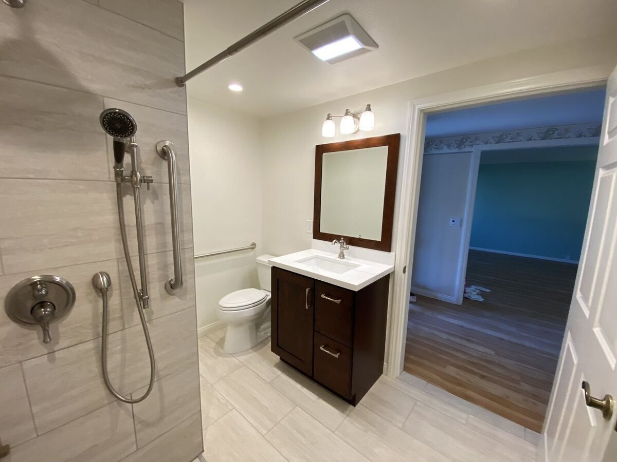Accessible shower with wall grab bars, hand shower and a wheelchair-height vanity alongside
