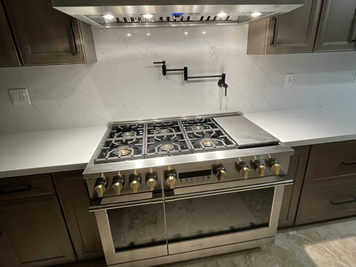 Pro range with brass knobs, a pot filler and a full-height quartz backsplash