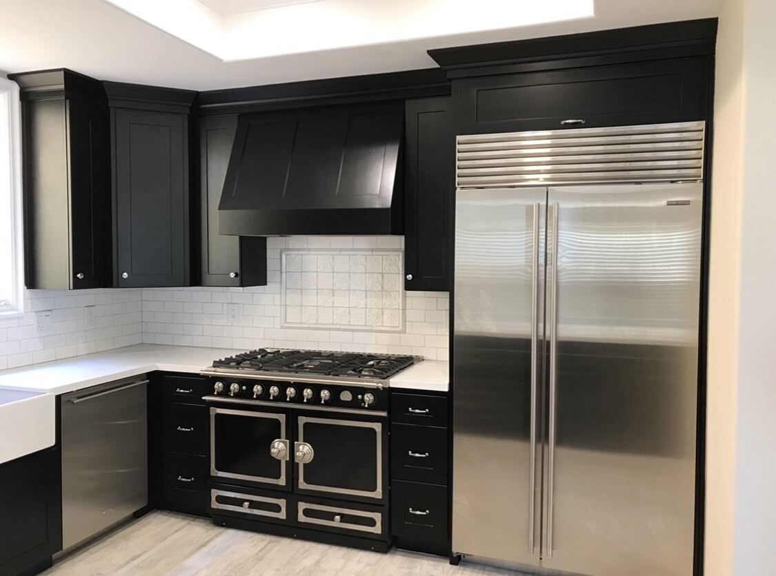 Finished kitchen with black shaker cabinetry, a panelled wood range hood, quartz counters and a professional range