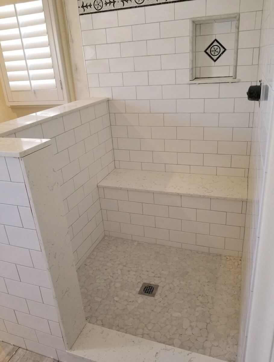 Walk-in shower with a full-width quartz bench, marble pebble floor and a subway-tile wall with a mosaic border