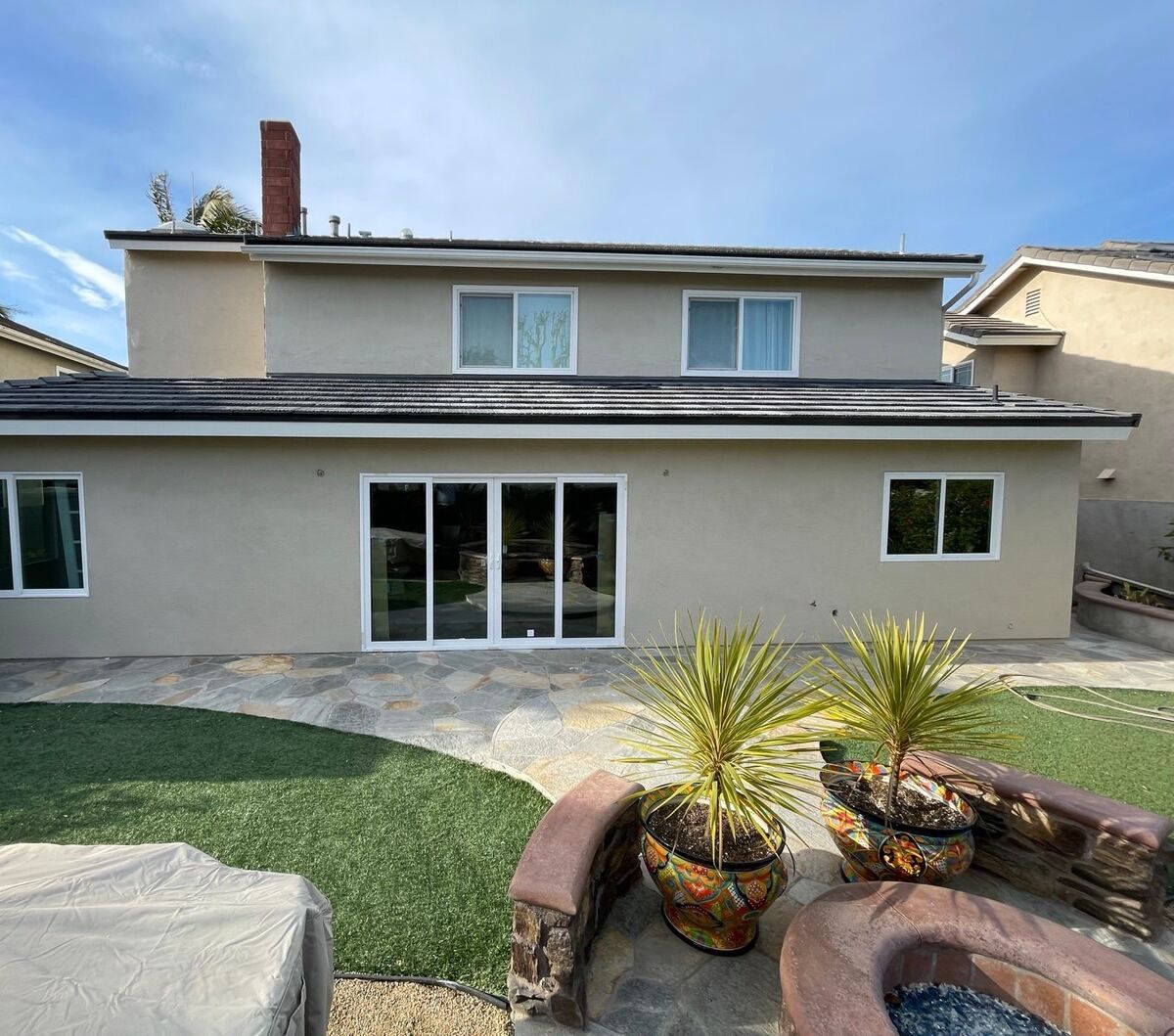 Rear of a two-story stucco house in Huntington Beach after the addition, with sliding doors onto a flagstone patio