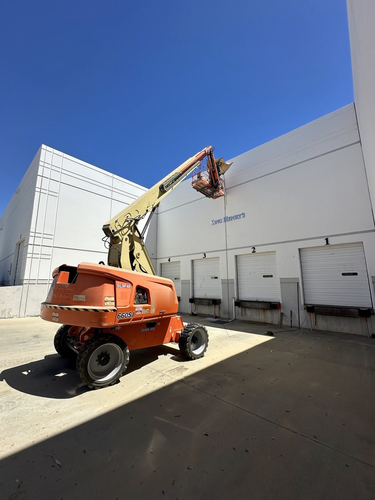 Boom lift raised to the King Henry's wall in Valencia, above four loading dock doors, under a clear blue sky