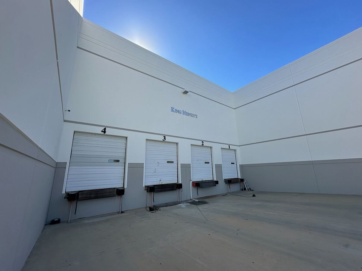 Loading dock court at King Henry's after the repair, with repainted white tilt-up wall panels and four numbered dock doors