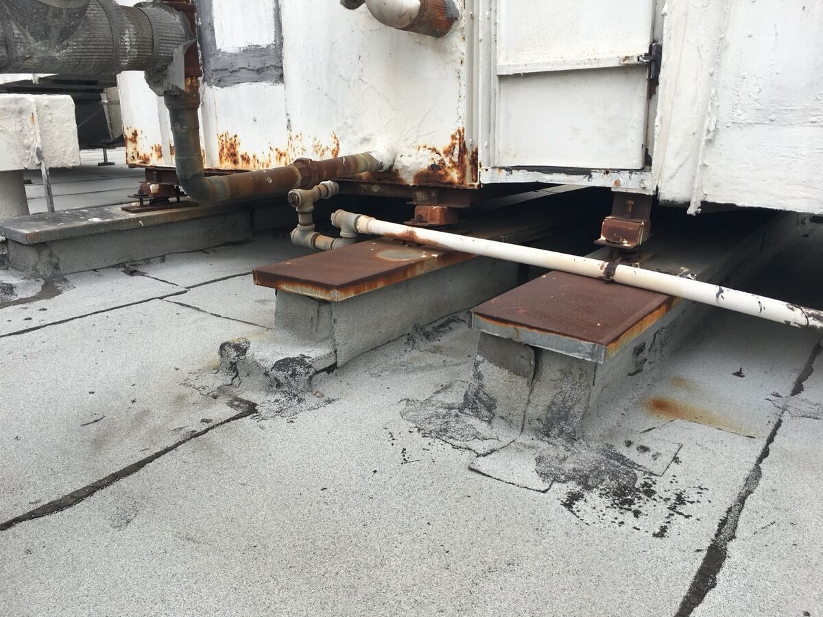 Rusted rooftop HVAC unit on rusted steel rails with mastic-patched roof penetrations