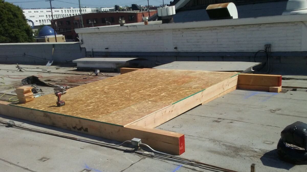 New wood-framed equipment platform with OSB decking under construction on a flat roof