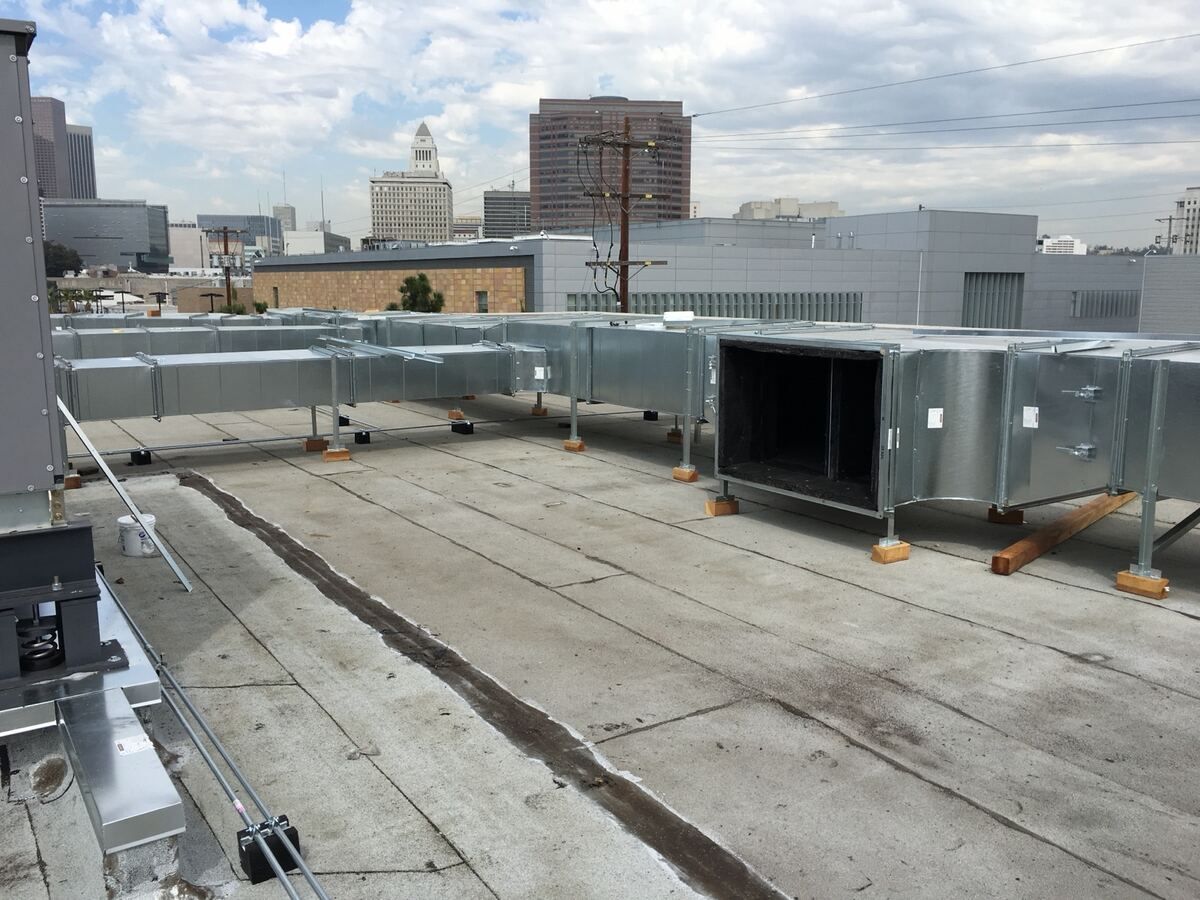 New galvanized ductwork on stanchions across a flat roof with the downtown Los Angeles skyline behind