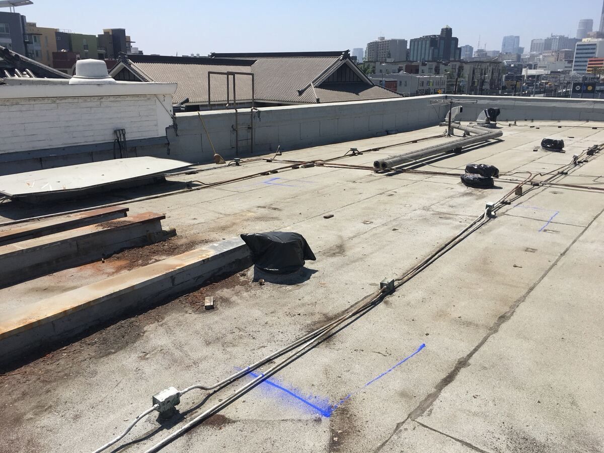 Old built-up roof with blue layout marks and surface-run conduit, temple tile roofs and downtown Los Angeles behind