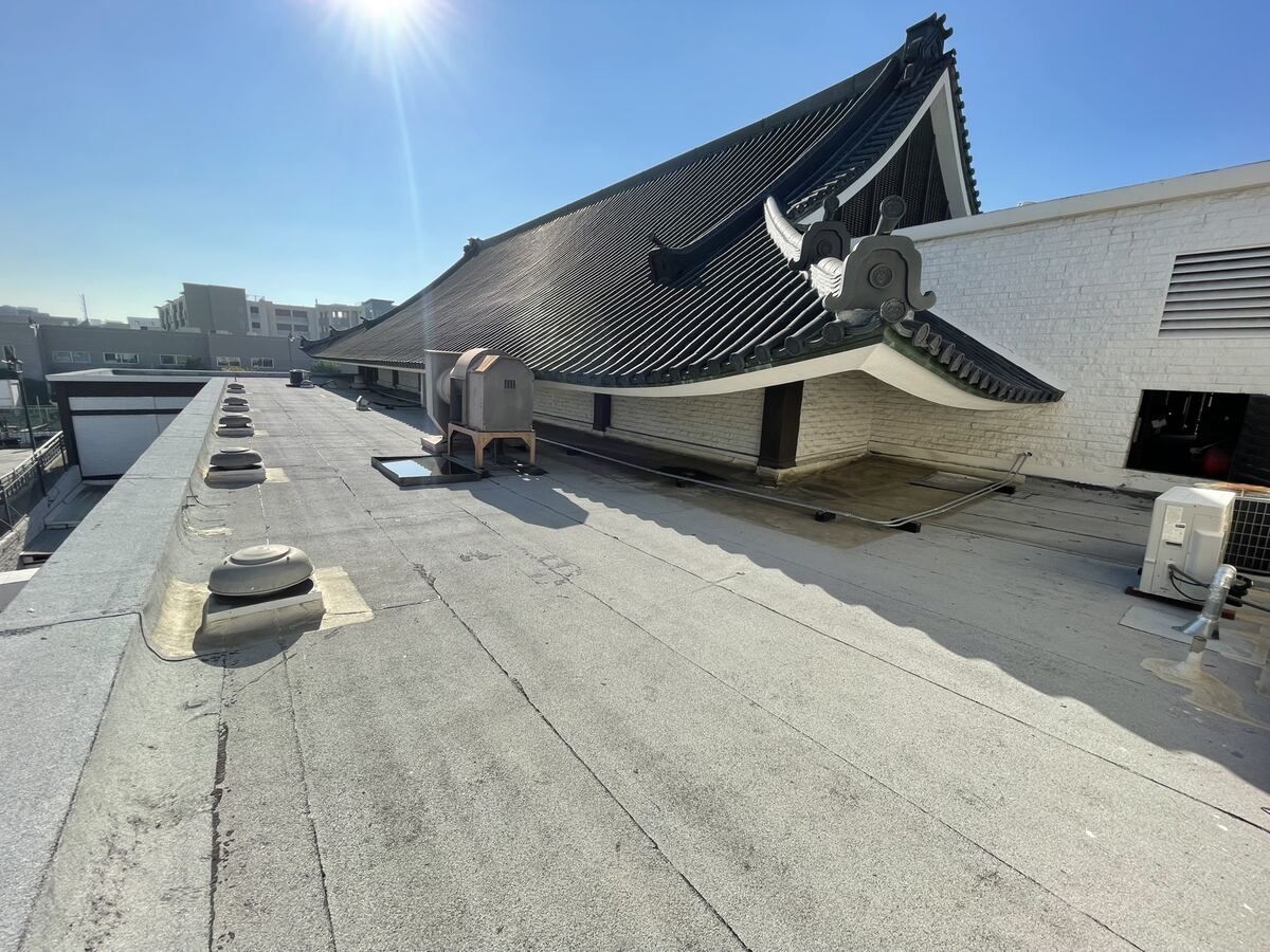 Nishi Hongwanji temple tile roof beside the flat roof, with turbine vents, an exhaust hood and a mini-split condenser