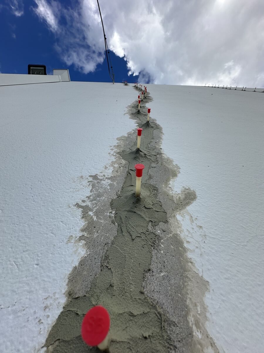 Line of red-capped epoxy injection ports set into a grey paste band along a crack running up a white tilt-up wall