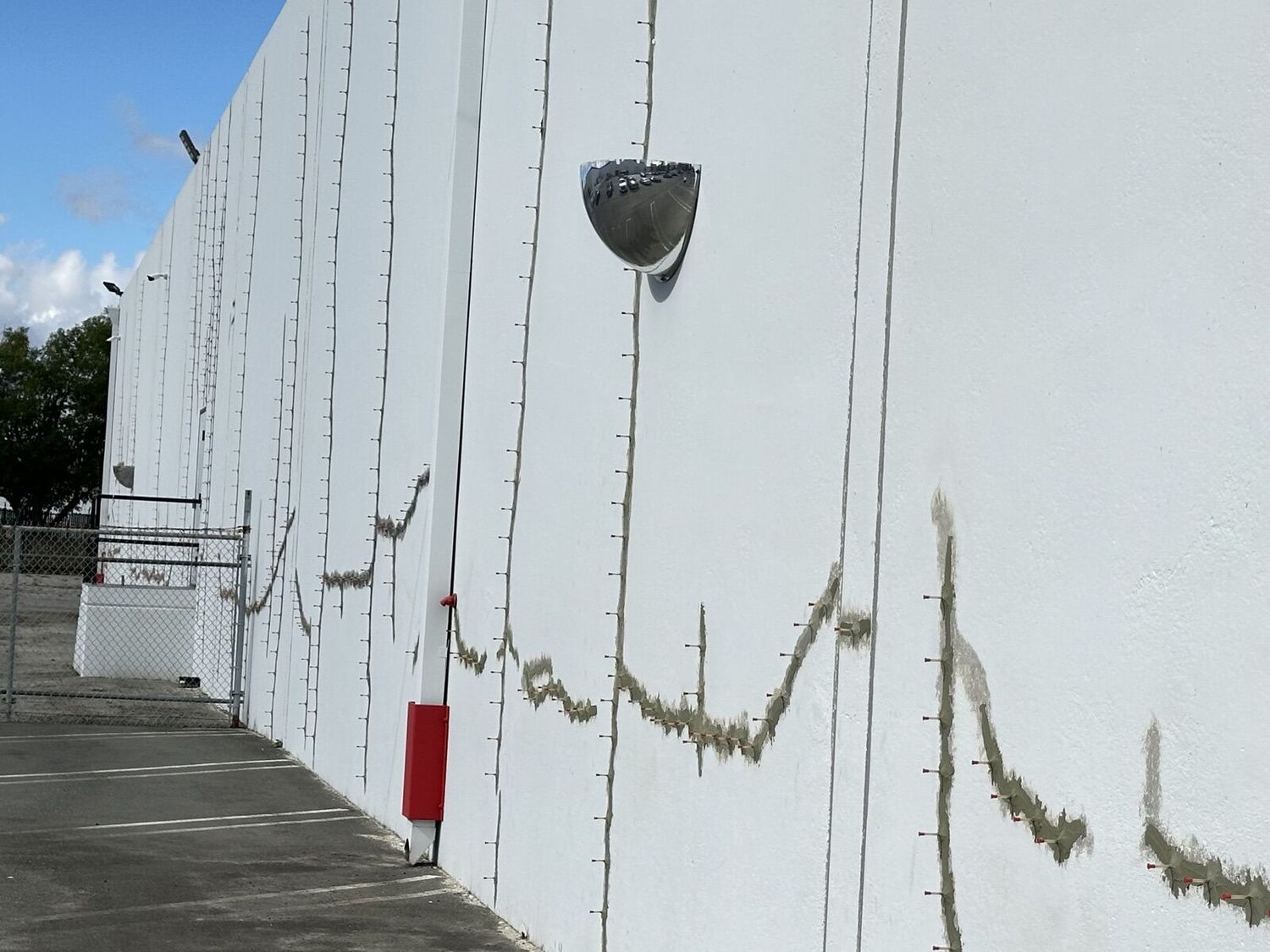 White tilt-up concrete wall with sealed and ported crack lines running down the panels, seen from the parking lot
