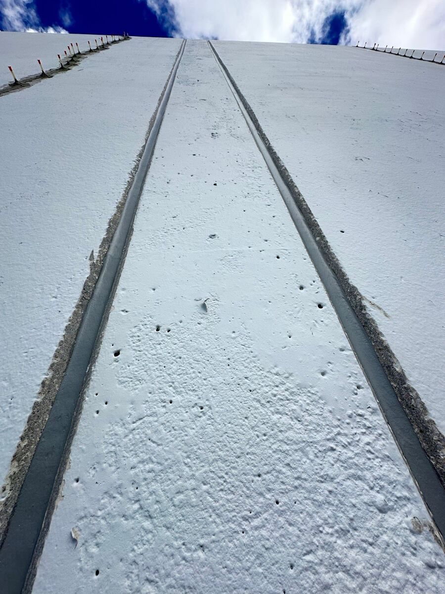 Grey sealant filling two straight vertical joints between white tilt-up wall panels, looking up the wall