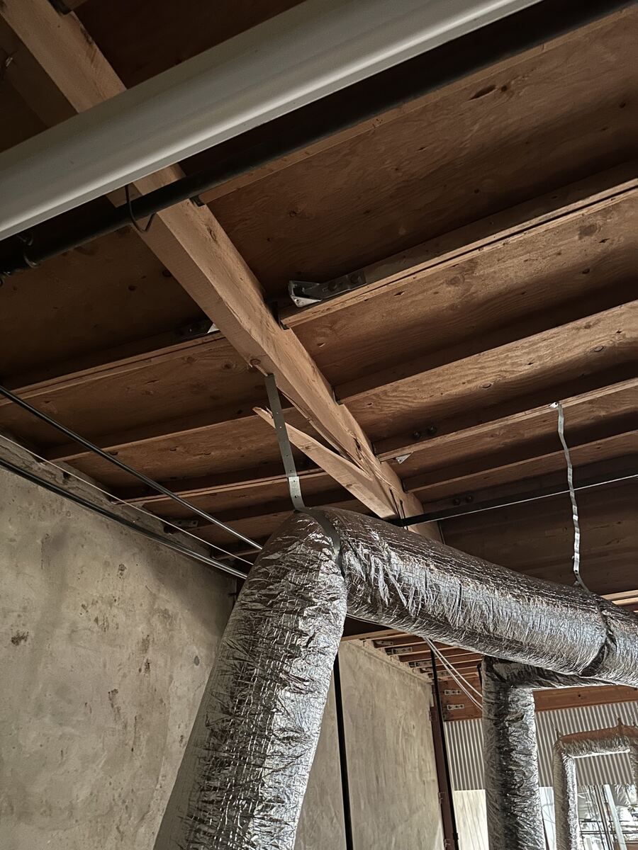 Wood framing member split along its length, with a metal strap tie crossing the break and insulated ductwork running past it