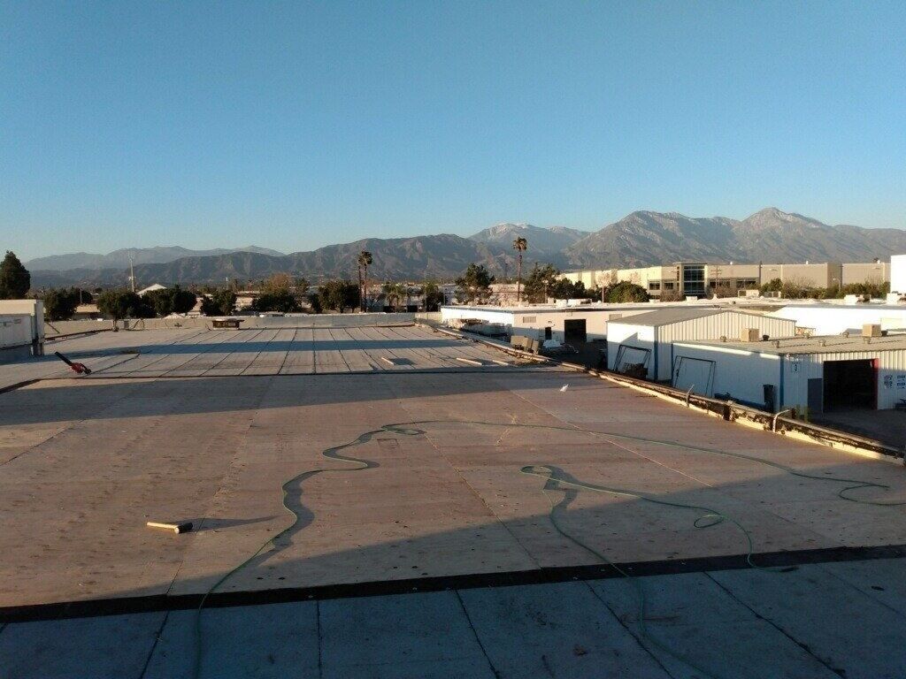 Worn brown commercial roof surface, patched and blistered, before replacement