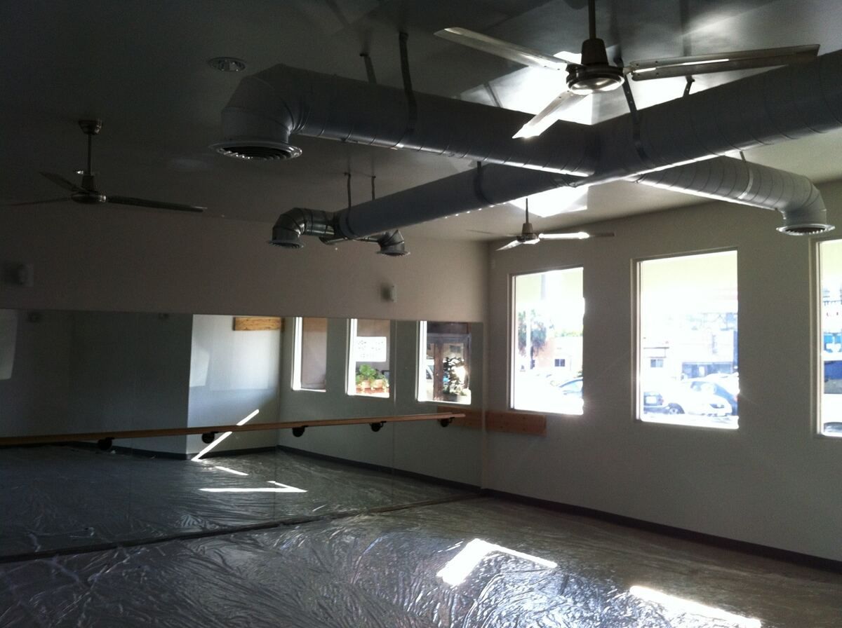 Room during finish work, with new spiral ductwork and ceiling fans overhead, mirrors and a wall-mounted rail in place, and the floor covered in protective plastic sheeting