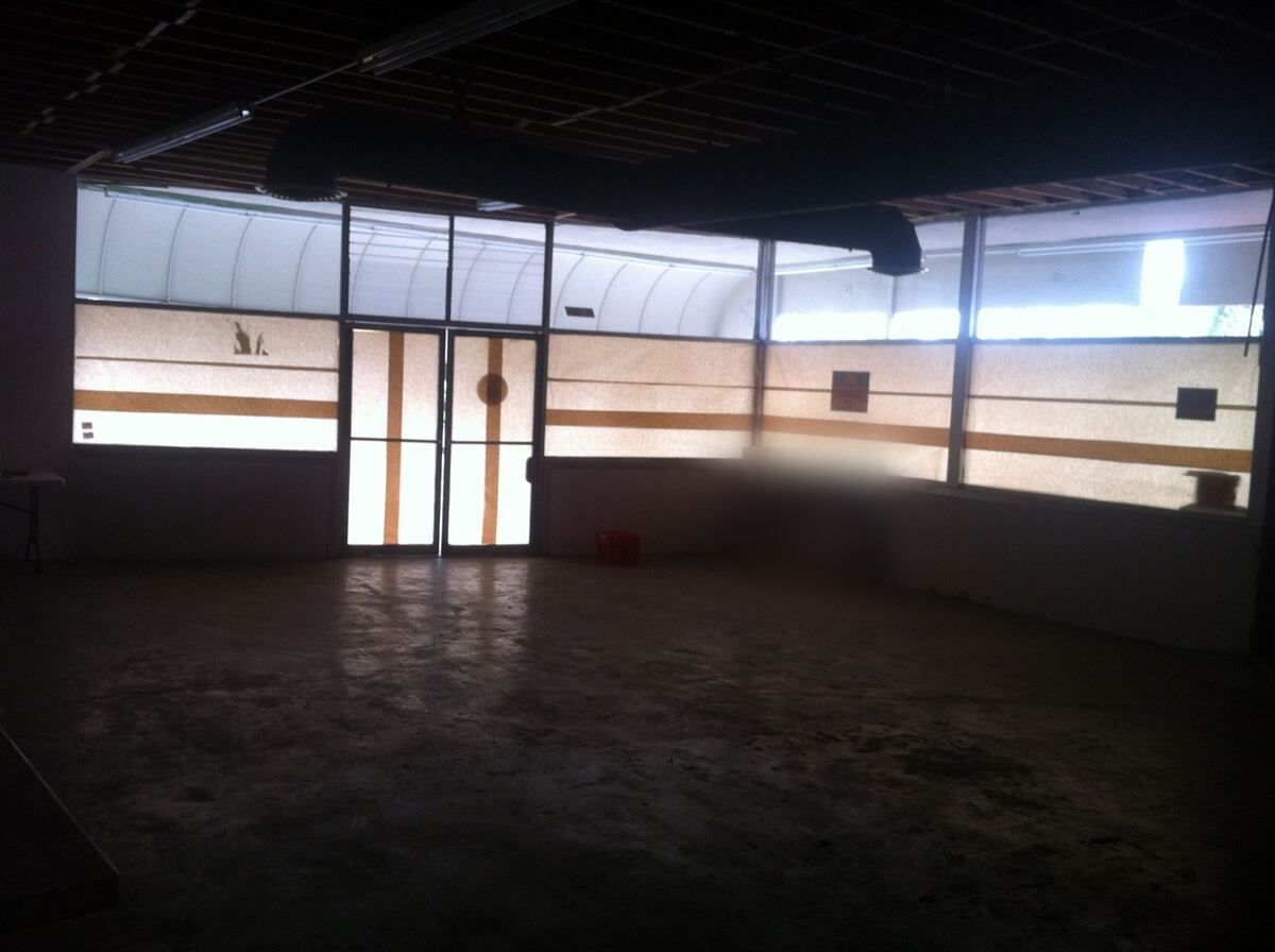 Empty commercial storefront before the build-out, with a bare concrete floor and papered-over glass storefront