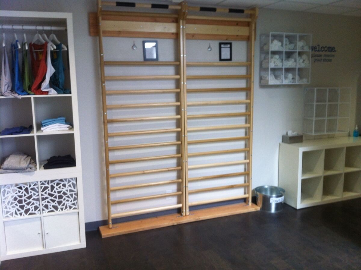 Finished lobby with two wooden wall bars anchored to the wall, white shelving units holding folded apparel and rolled towels, and a dark wood-plank floor